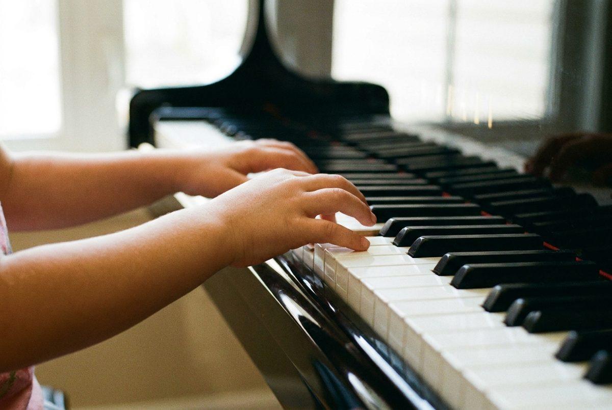 A young child's hands with correctly curved fingers on the keys of a black grand piano