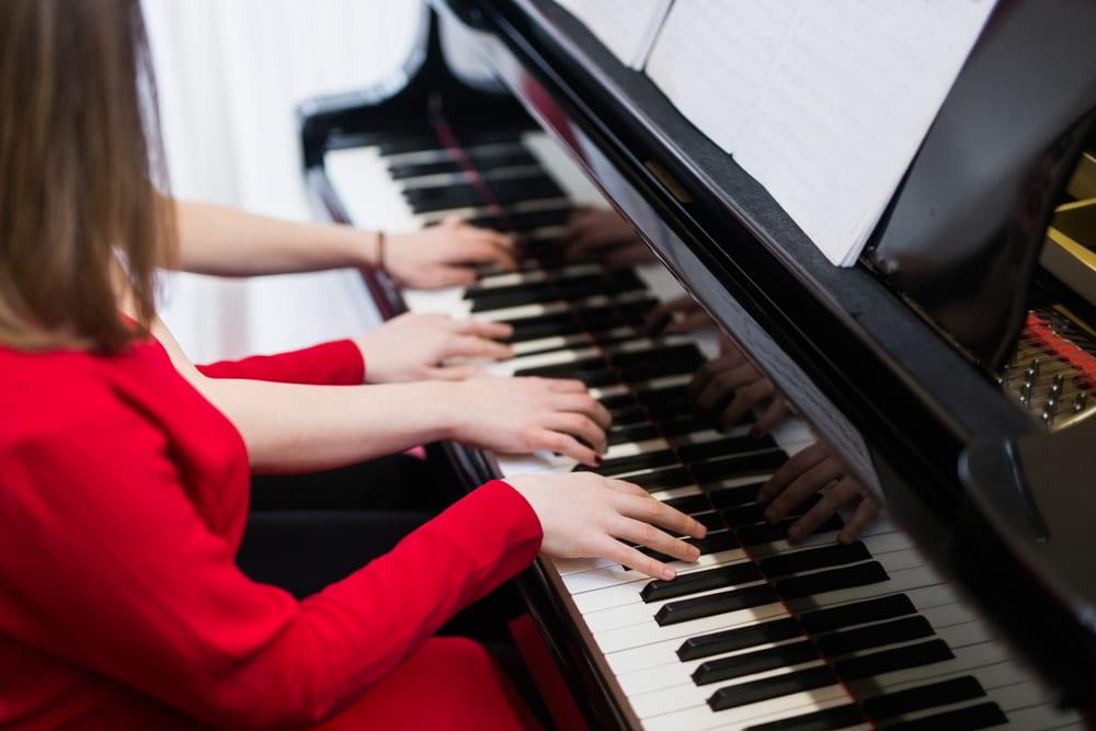Two pianists playing a duet at the same grand piano, four hands together on the keys