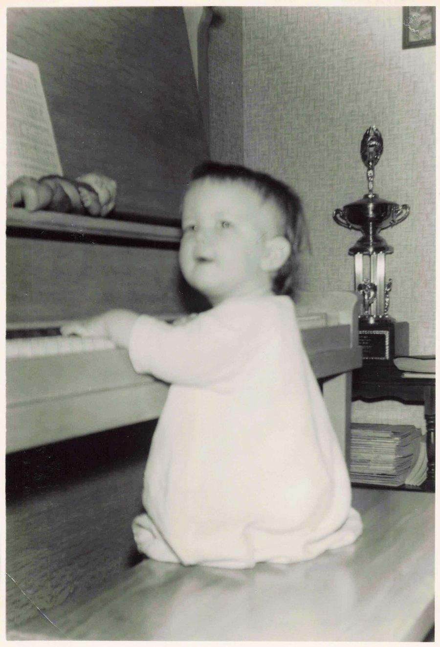 Judy as a very young child reaching up to the keys of an upright piano in 1959